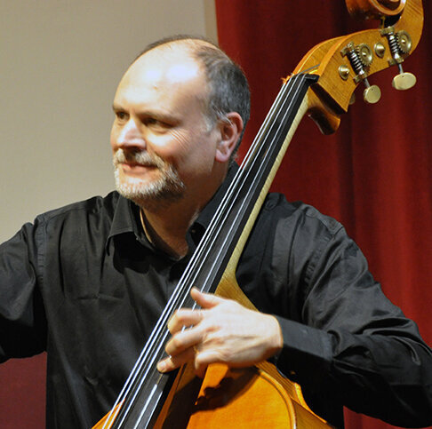 L'image montre un contrebassiste en train de jouer, avec un sourire et une attitude détendue. L'instrumentiste semble apprécier son jeu, illustrant l'importance de la passion et de la technique dans la performance musicale avec un archet de contrebasse français 32 mm.