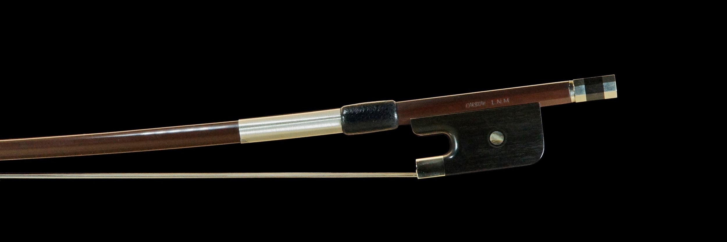 Cette image présente une vue latérale complète de l'archet de contrebasse français avec une baguette brune de 32mm. La combinaison de la baguette brune et de la hausse en ébène, associée aux finitions métalliques, met en évidence la qualité et la précision de la fabrication de cet archet.