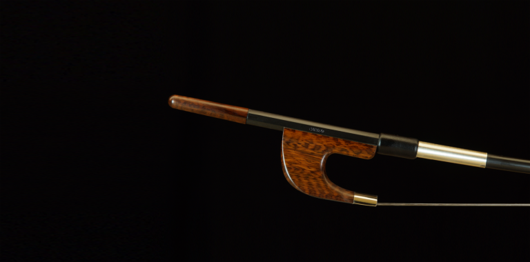 L'image montre un archet de contrebasse de style allemand, reconnaissable à sa forme distincte et à son design en bois finement travaillé. Les german double bass bows sont appréciés pour leur robustesse et leur capacité à produire un son riche et puissant, adapté aux besoins des contrebassistes dans divers genres musicaux.
