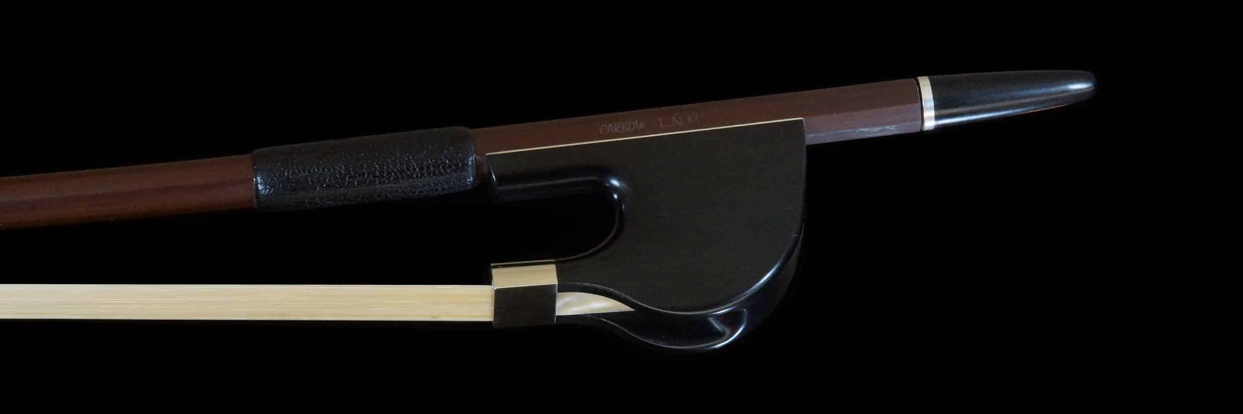 L'image montre un archet hybride pour contrebasse, combinant des matériaux traditionnels en bois avec des éléments modernes pour une meilleure performance et durabilité. Cet archet est conçu pour offrir une réponse précise et une maniabilité optimale